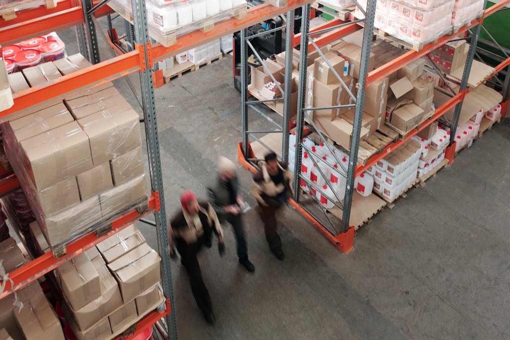 A high angle view of workers in motion in a busy warehouse with shelves full of boxes and packages.